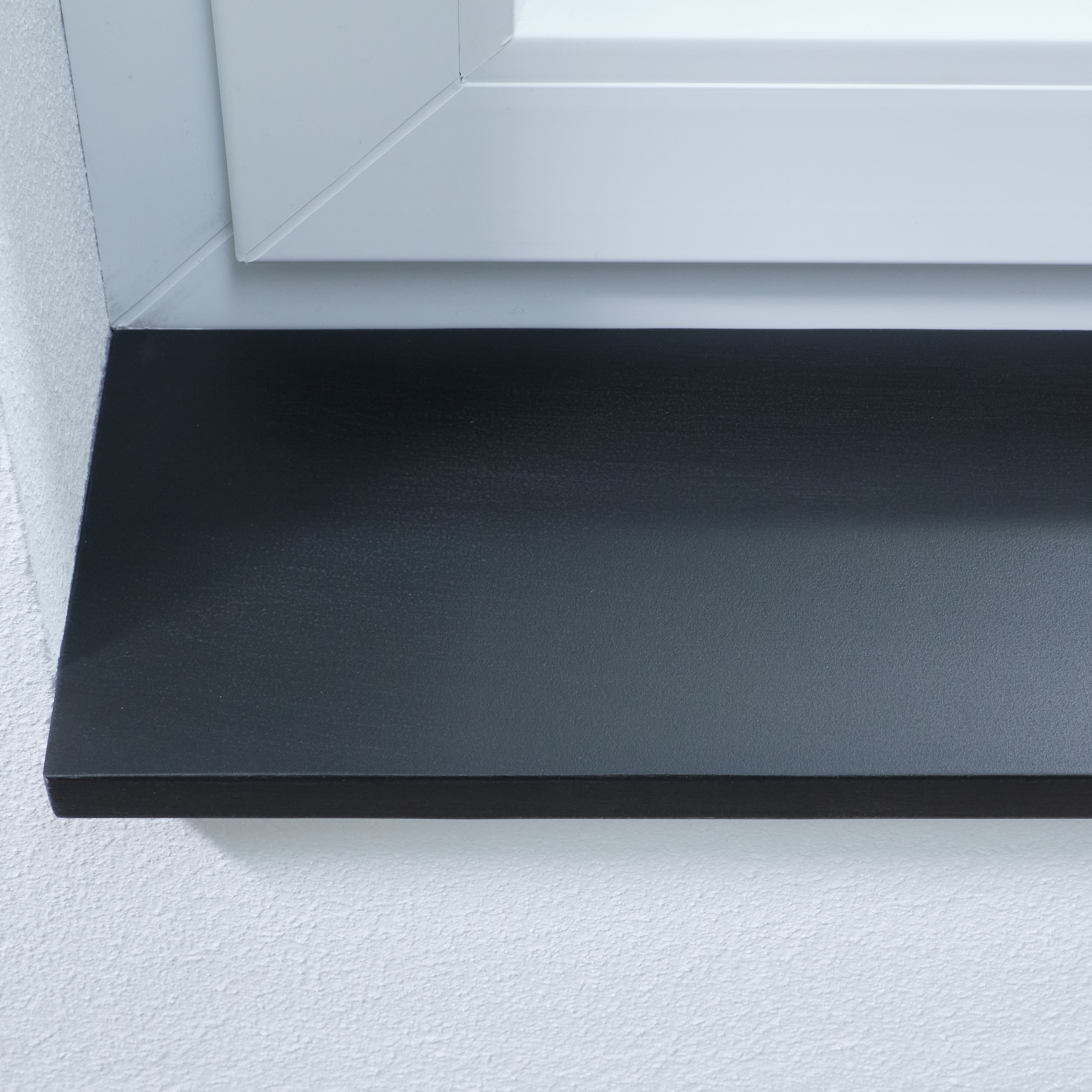 Davanzale nero in legno massello, primo piano del bordo anteriore e della superficie sotto un telaio di finestra bianco