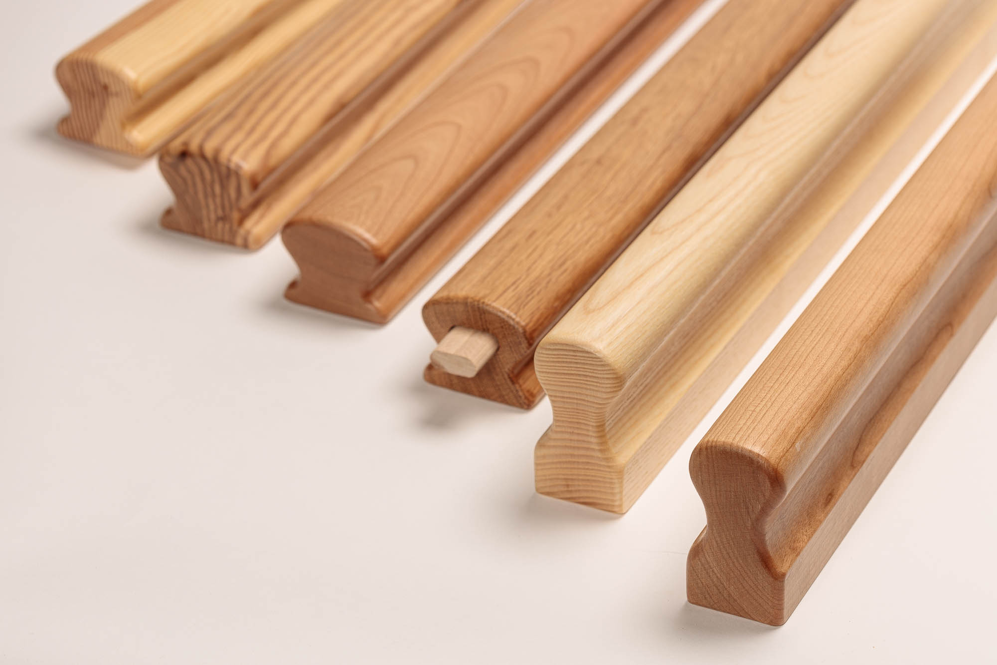 Corrimano in legno Omega in sei essenze affiancati, legni da chiari a rossastri, profilo omega con incavo di presa visibile