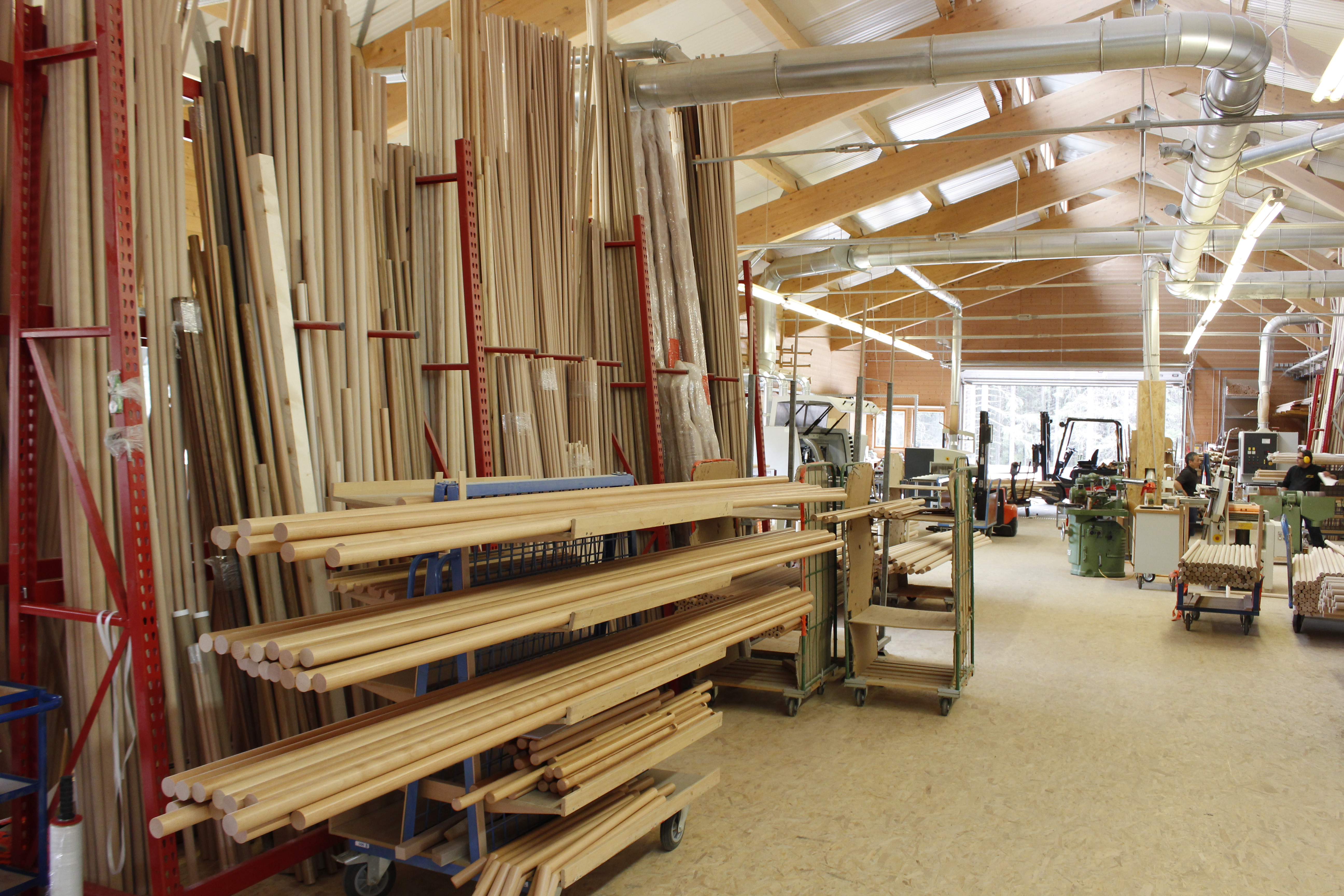 Corrimano in legno e tondini nel magazzino della tornitura, lunghe aste di legno su scaffali cantilever rossi nel capannone