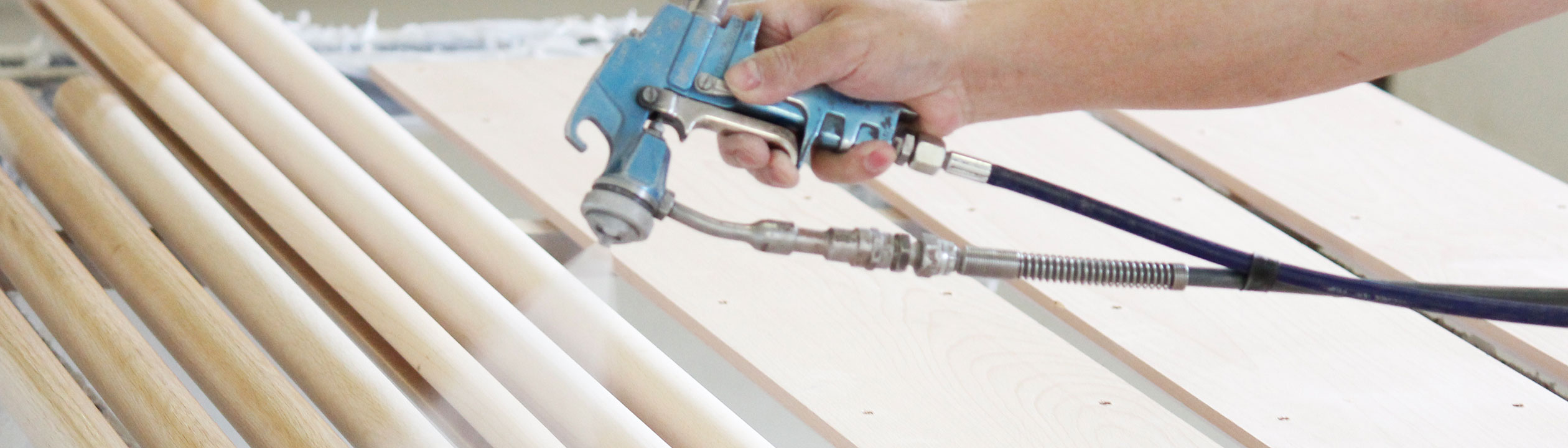 Produzione di corrimano: corrimano in legno verniciati con pistola a spruzzo, mano con la pistola sopra aste di legno chiaro