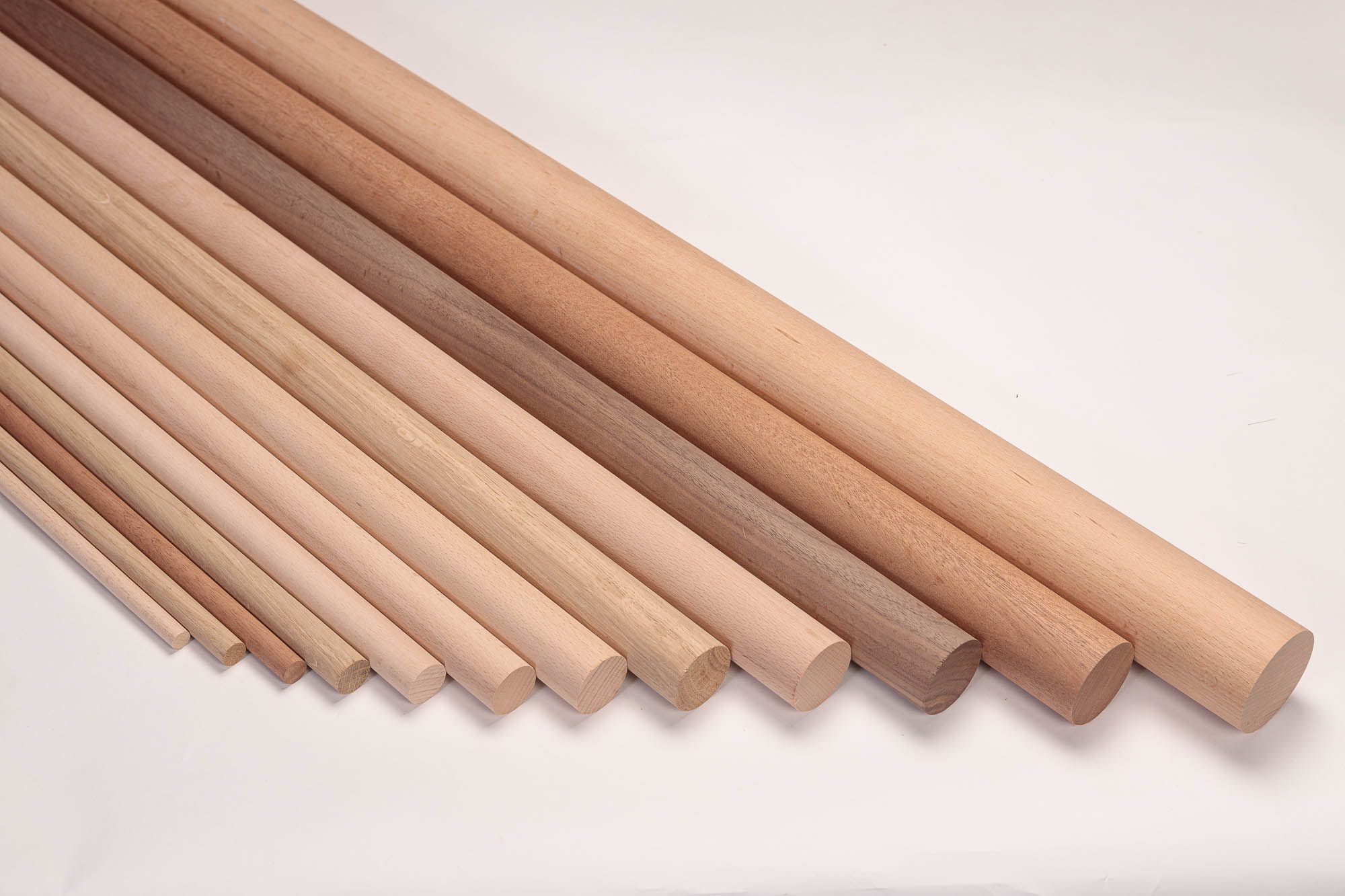 Barre tonde in legno di diversi diametri ed essenze disposte a scalare una accanto all'altra, legni da chiari a rossastri