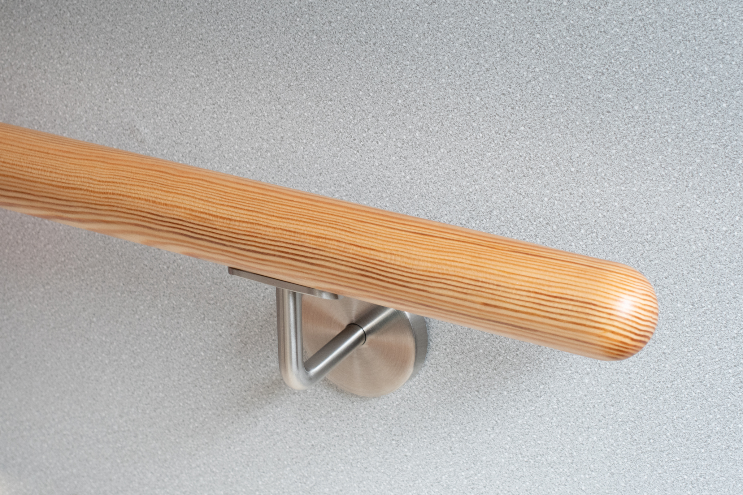 Corrimano rotondo in pino con supporto inox su parete grigio chiaro, legno di conifera con venatura visibile, primo piano