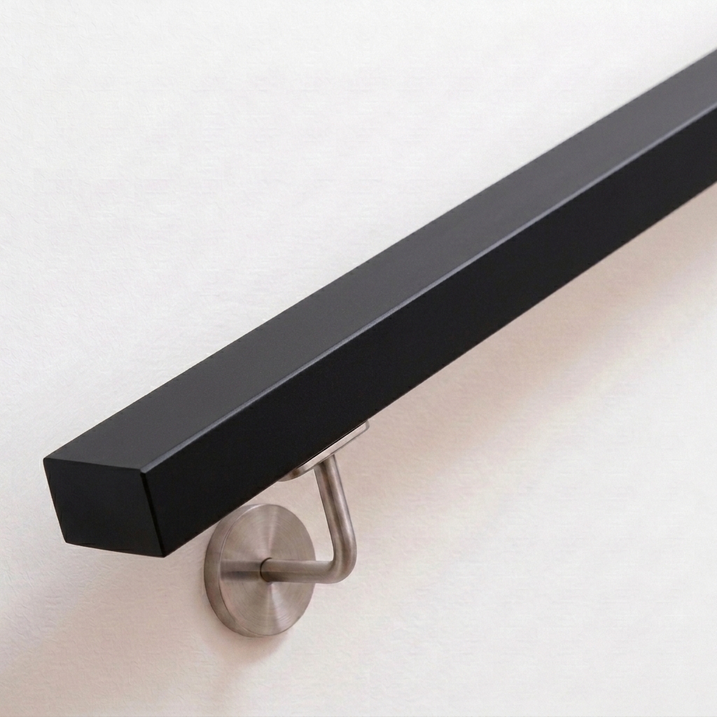 Corrimano rettangolare in faggio verniciato nero, supporto in acciaio inox su parete bianca, estremità dritta, vista obliqua