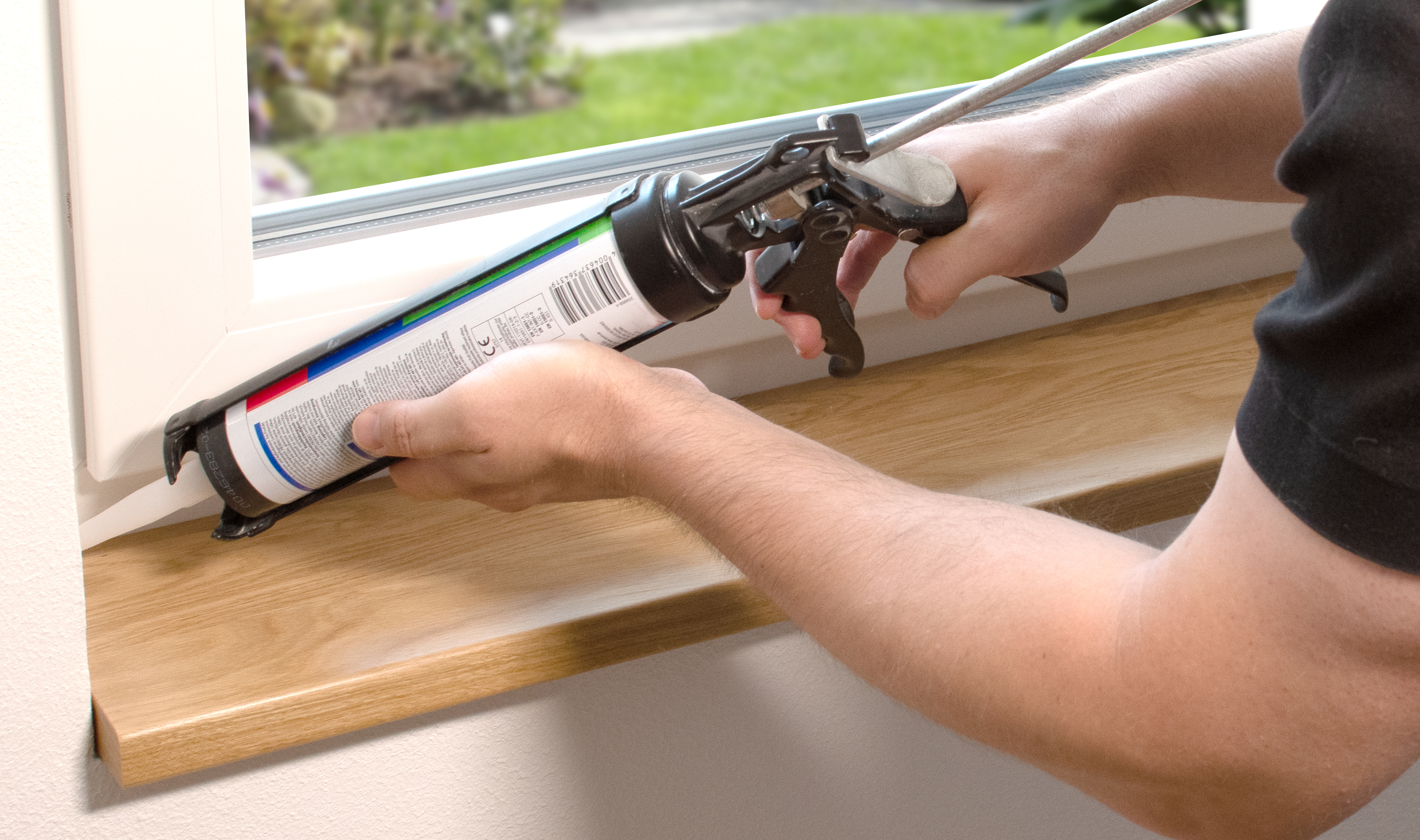 Davanzale in legno da sigillare: le mani stendono con la pistola un giunto di silicone tra davanzale e finestra