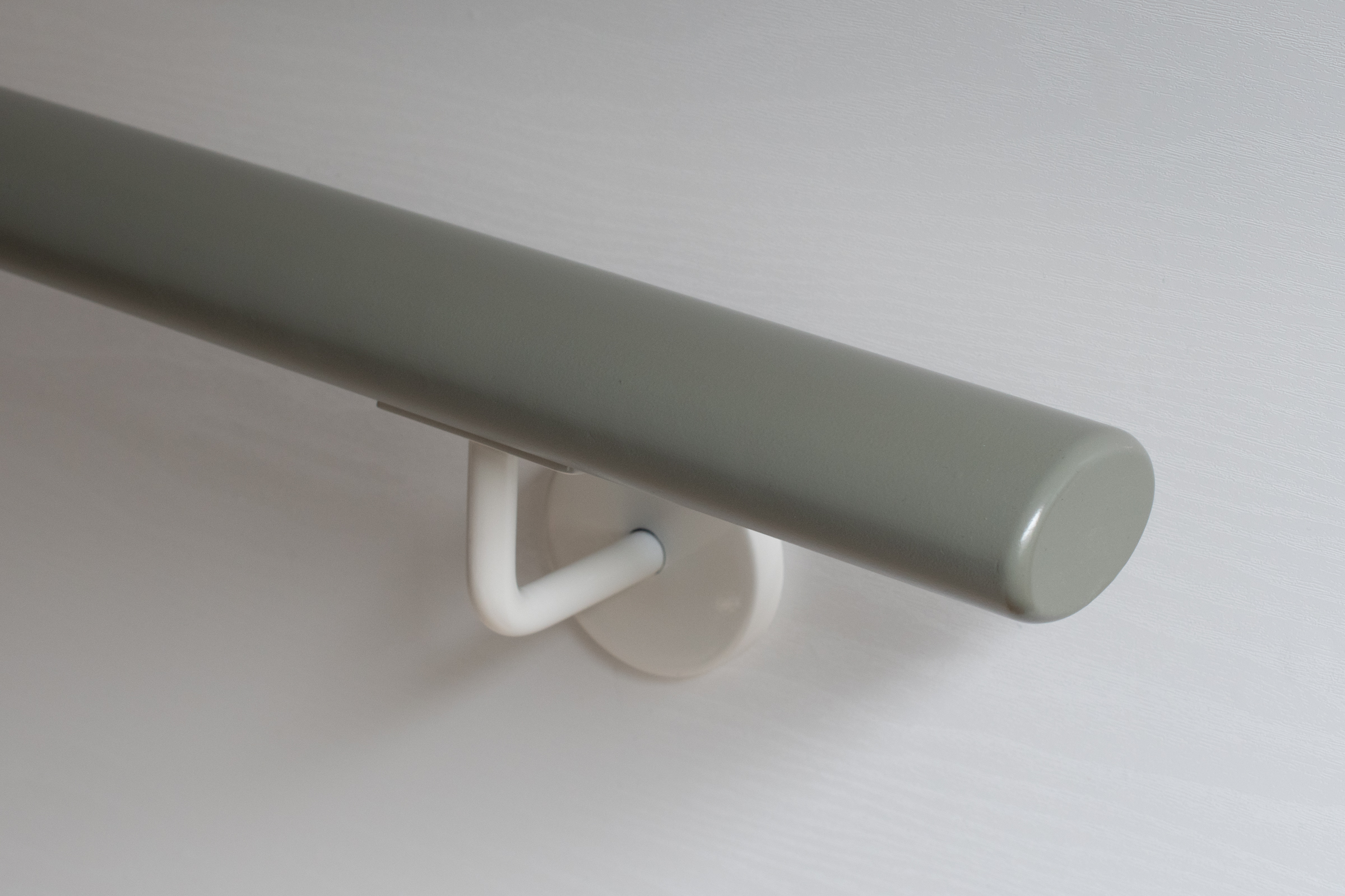 Corrimano rotondo in legno verniciato grigio con supporto bianco su parete bianca, primo piano dell'estremità rotonda