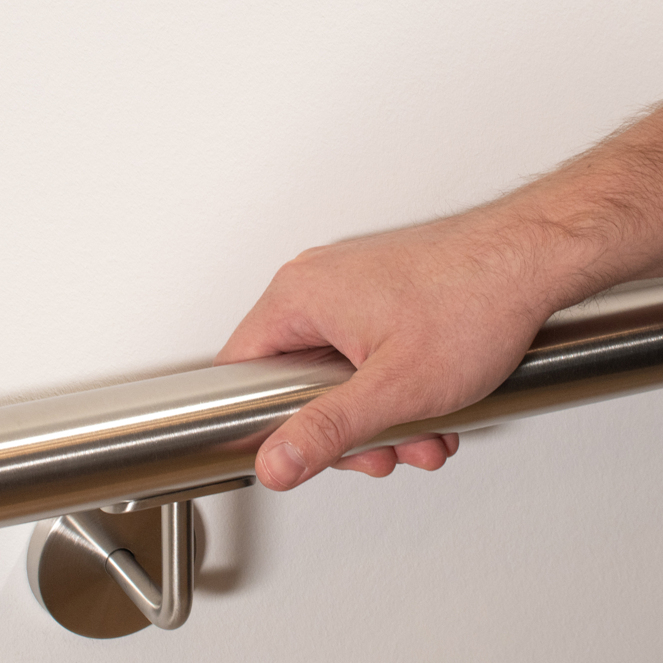 Corrimano rotondo in acciaio inossidabile su parete bianca con supporto inox, una mano impugna il corrimano, primo piano