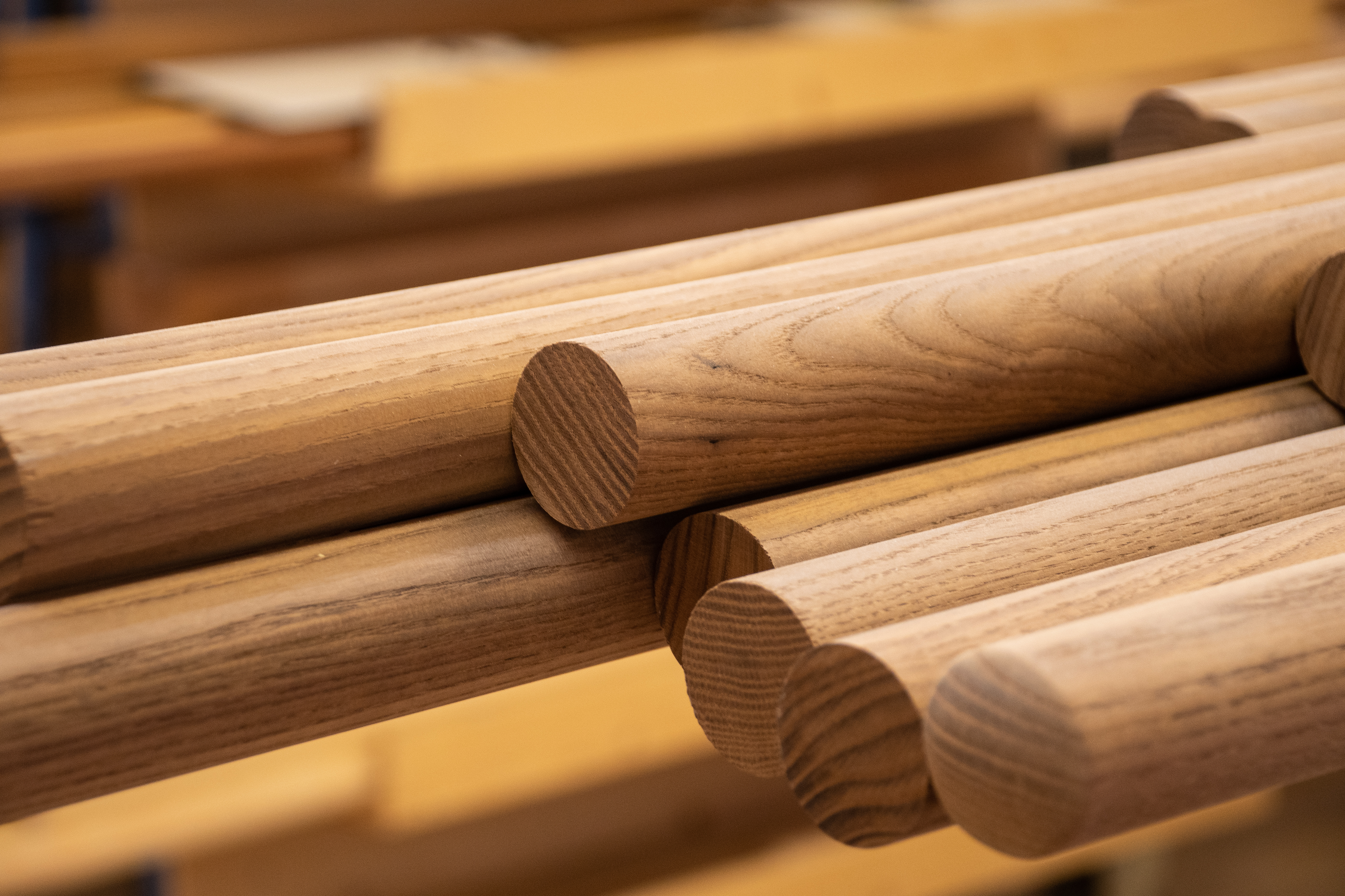 Corrimano in legno rotondi impilati sullo scaffale dell'officina, aste tonde con testate e venatura visibili, primo piano