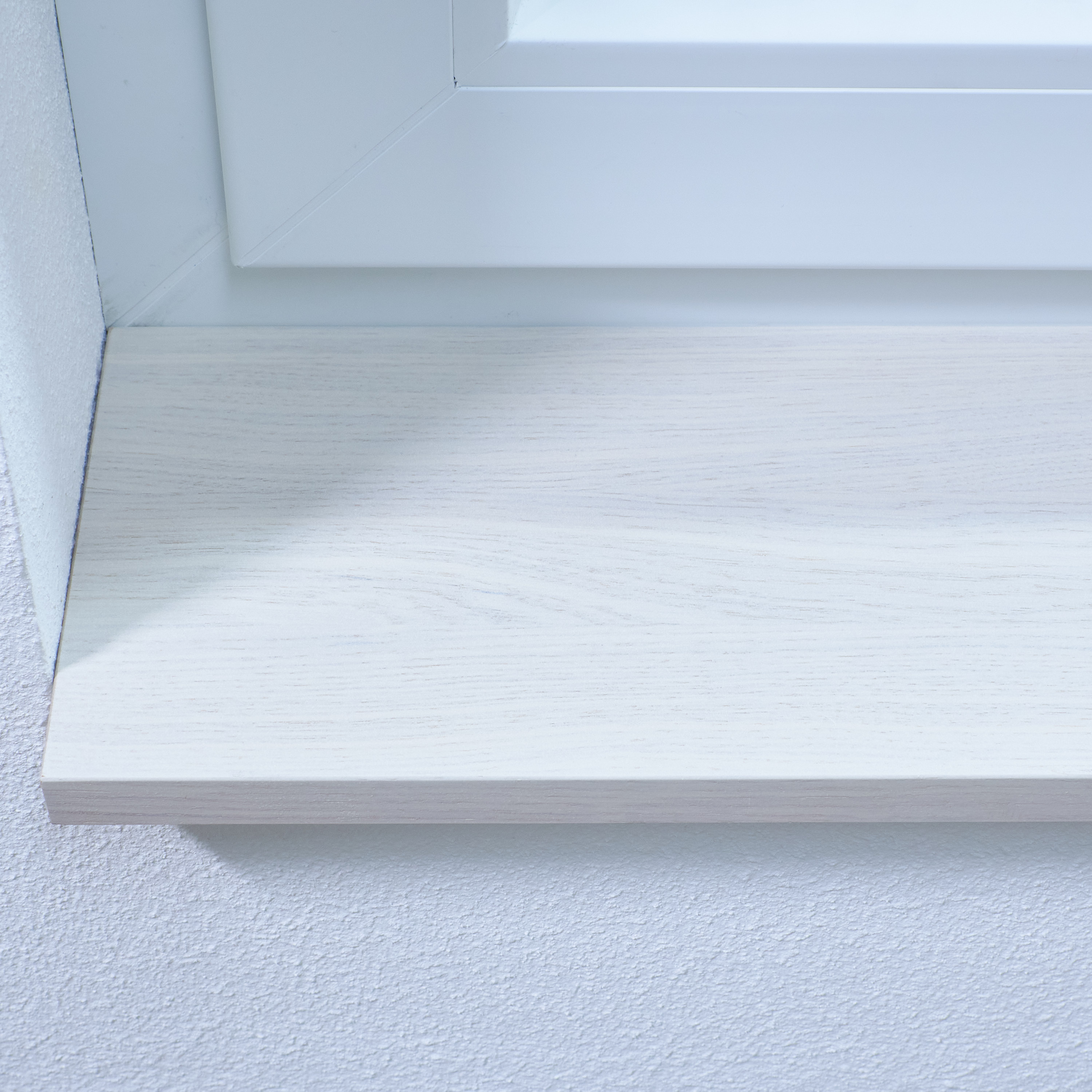 Davanzale tinto bianco con venatura del legno visibile, primo piano del bordo anteriore sotto un telaio di finestra bianco