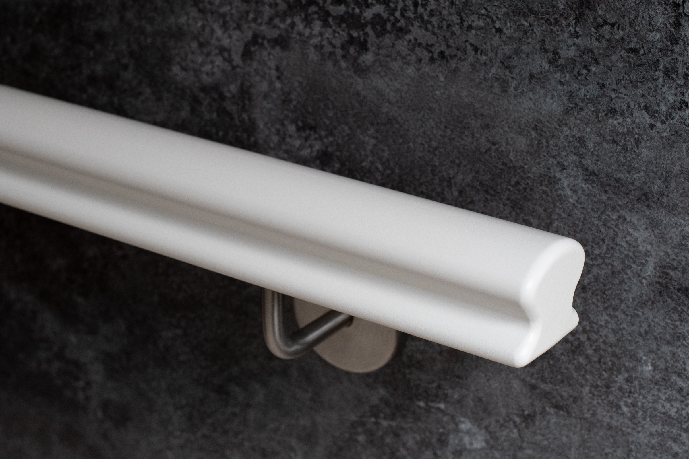 Corrimano Omega in legno verniciato bianco con supporto a parete inox su parete grigio scuro, primo piano del profilo
