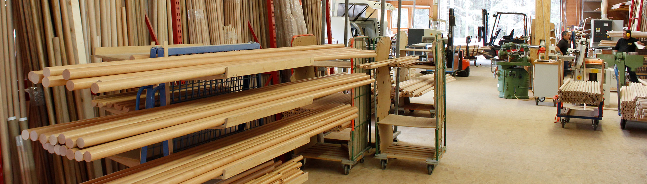 Produzione di corrimano: magazzino con corrimano in legno chiaro e tondini su carrelli nel laboratorio, formato banner
