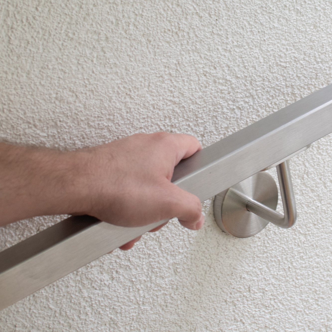 Corrimano quadrato in acciaio inossidabile su parete intonacata, mano che lo impugna, supporto a parete inox con rosetta