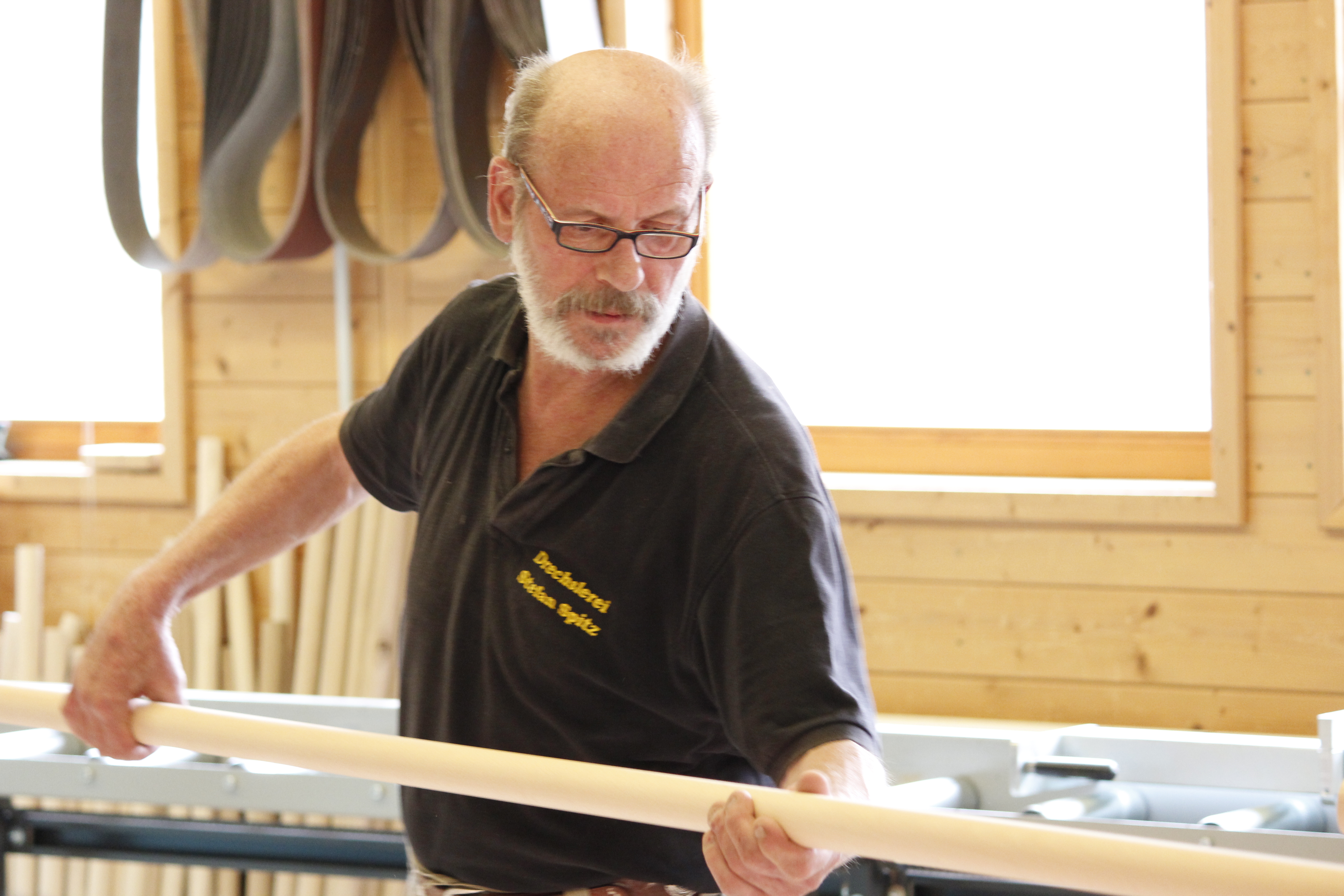 Produzione di corrimano: addetto controlla un corrimano in legno rotondo in officina, parete di legno e banco da lavoro