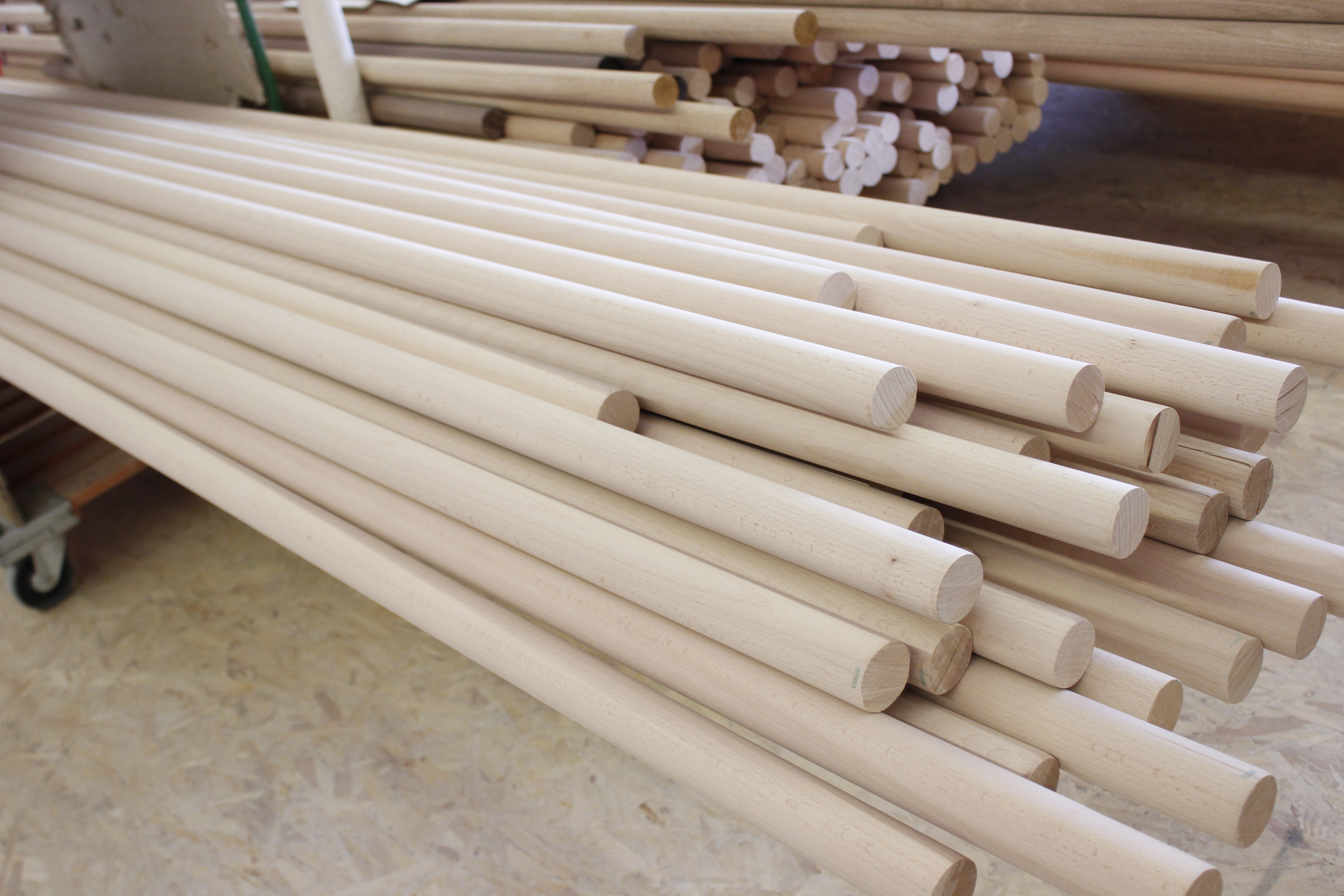 Corrimano in legno rotondi grezzi impilati su un carrello nel laboratorio, legno chiaro non trattato senza finitura