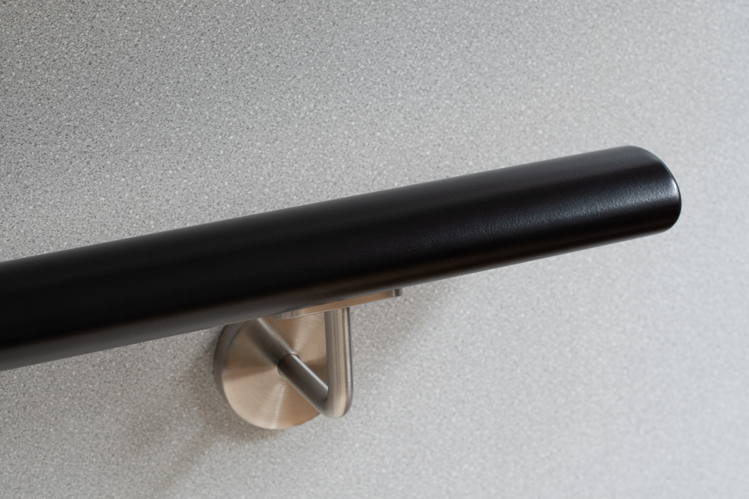 Corrimano rotondo in legno verniciato nero con supporto inox su parete grigia, primo piano dell'estremità arrotondata