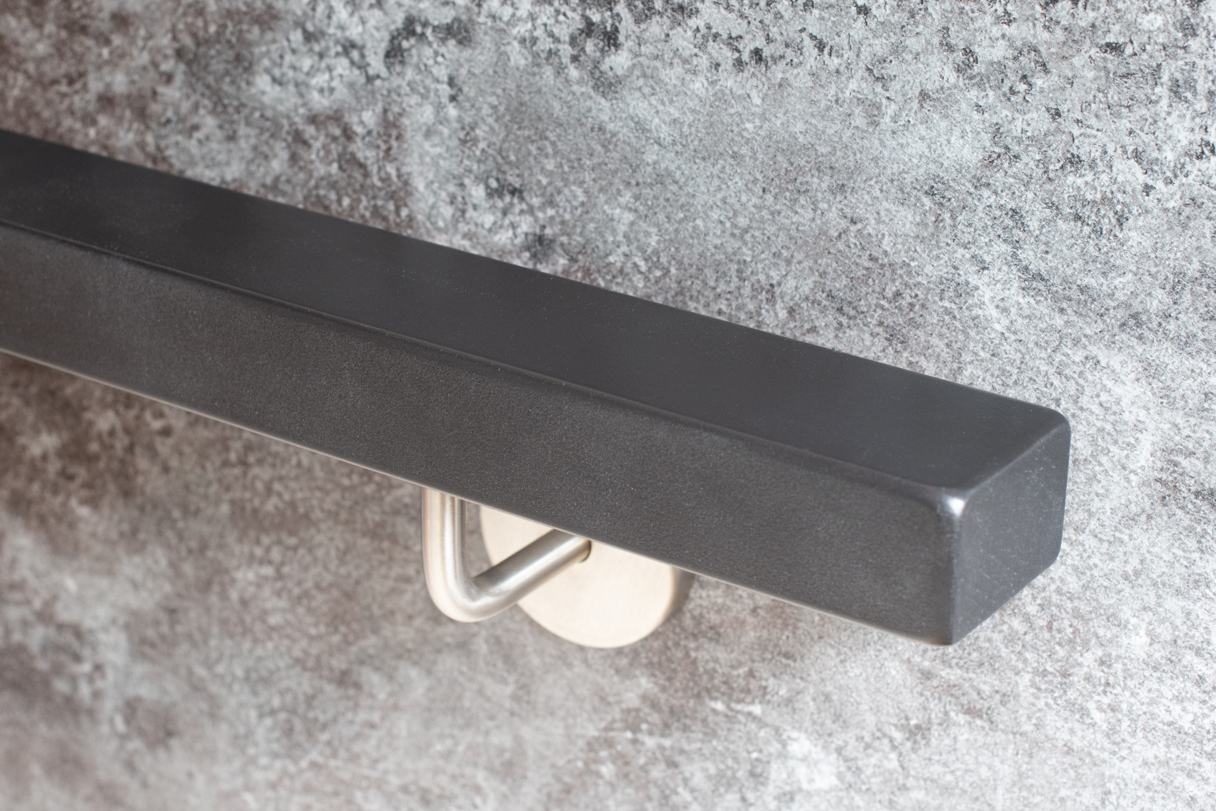 Corrimano rettangolare verniciato grigio con supporto inox su parete in pietra grigia, estremità diritta, vista obliqua