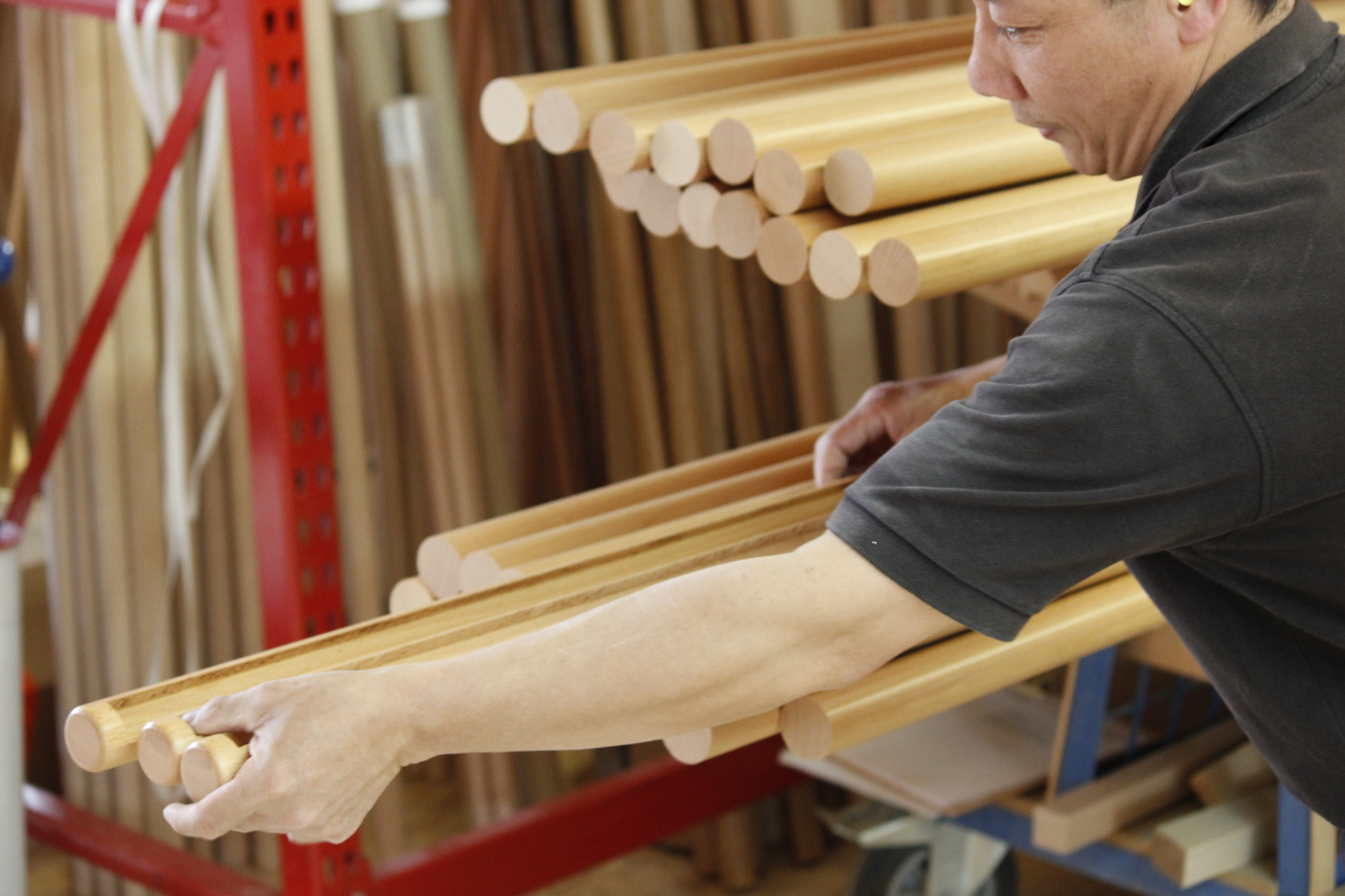 Corrimano rotondi in faggio in fascio, portati da un addetto in officina, scaffale con aste di legno sullo sfondo