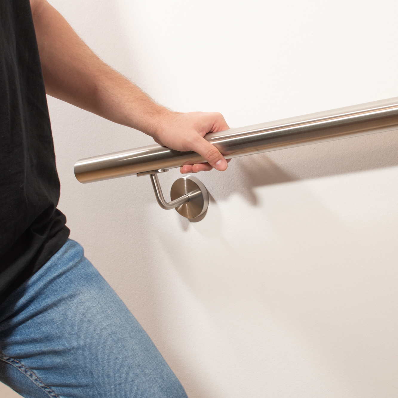 Corrimano rotondo in acciaio inossidabile su parete bianca con supporto inox, persona in jeans si tiene al corrimano