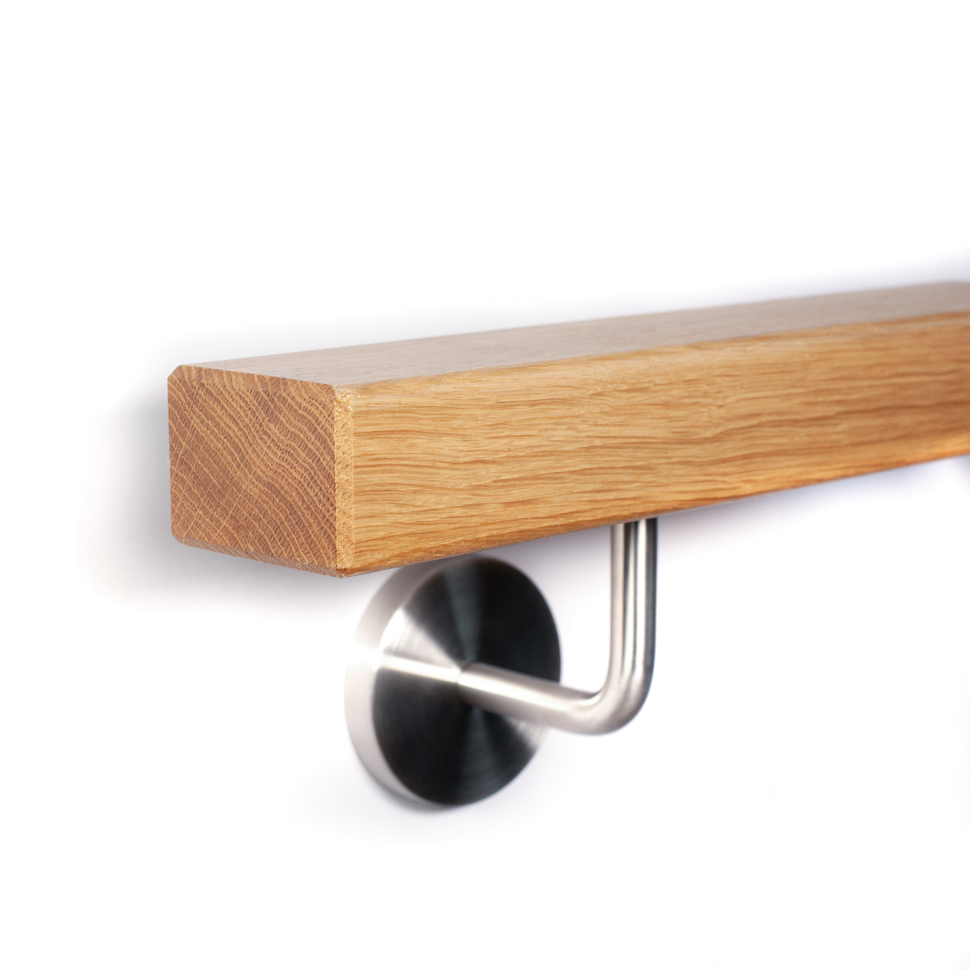 Corrimano rettangolare in rovere con smusso e supporto a parete inox con rosetta su parete bianca, primo piano dal basso